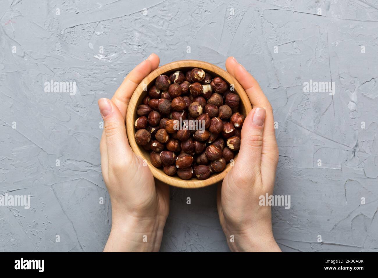 Woman hands holding a wooden bowl with hazelnut nuts. Healthy food and ...