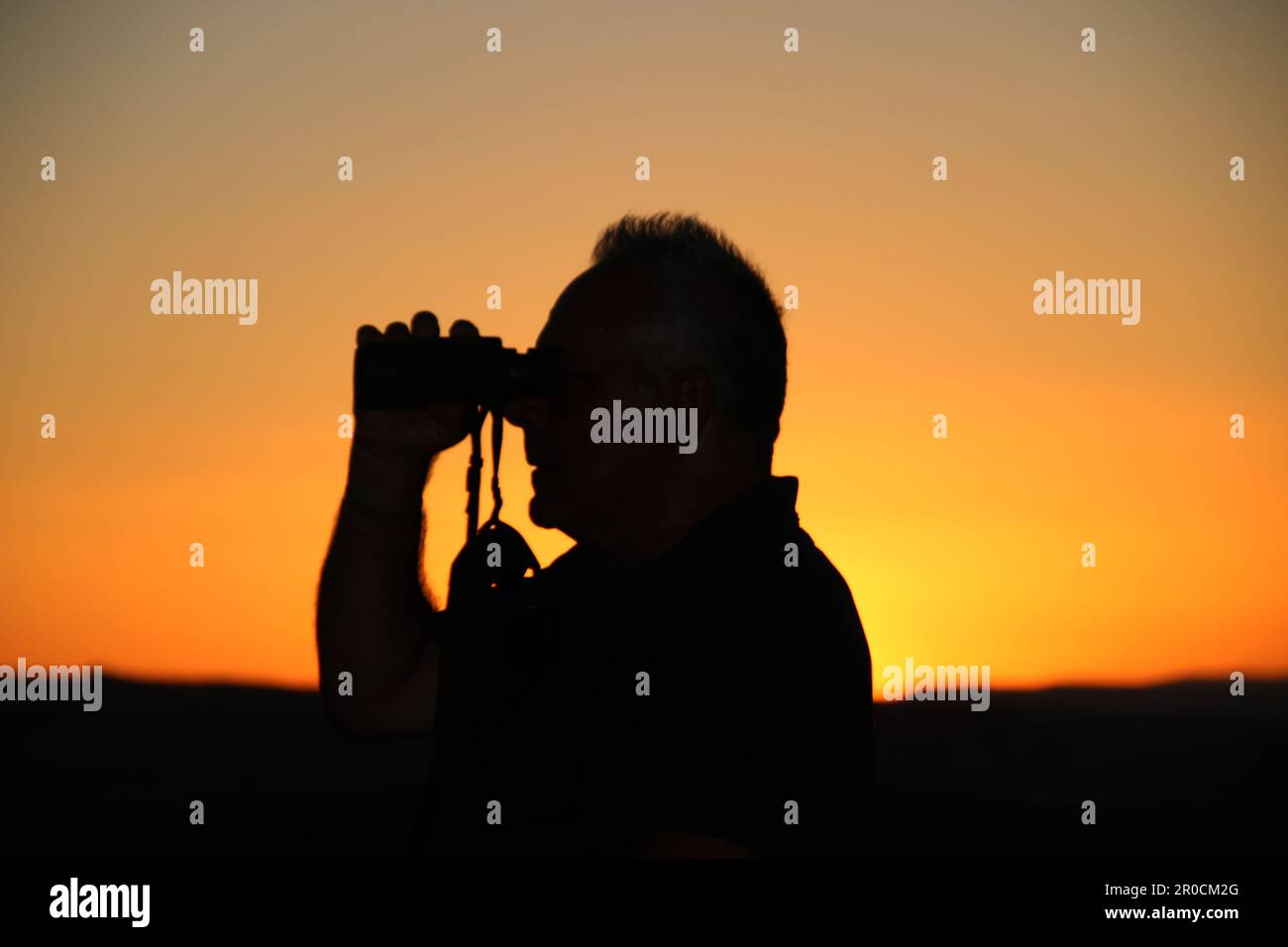 Silhouette of a profile of a man looking through binoculars at sunset Stock Photo