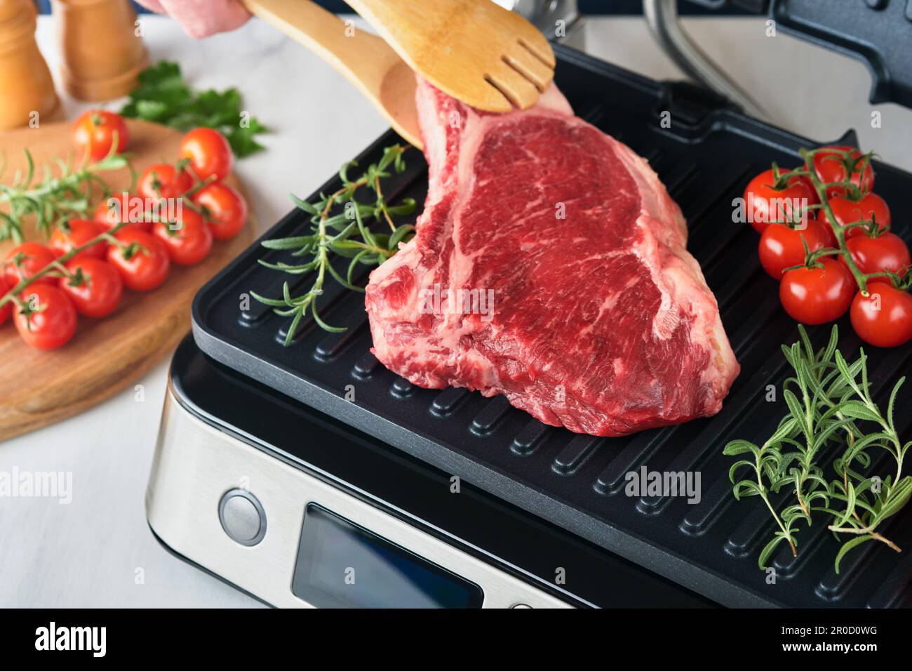 Raw prime steaks on electric grill. Chef male hand holding steak Ribeye