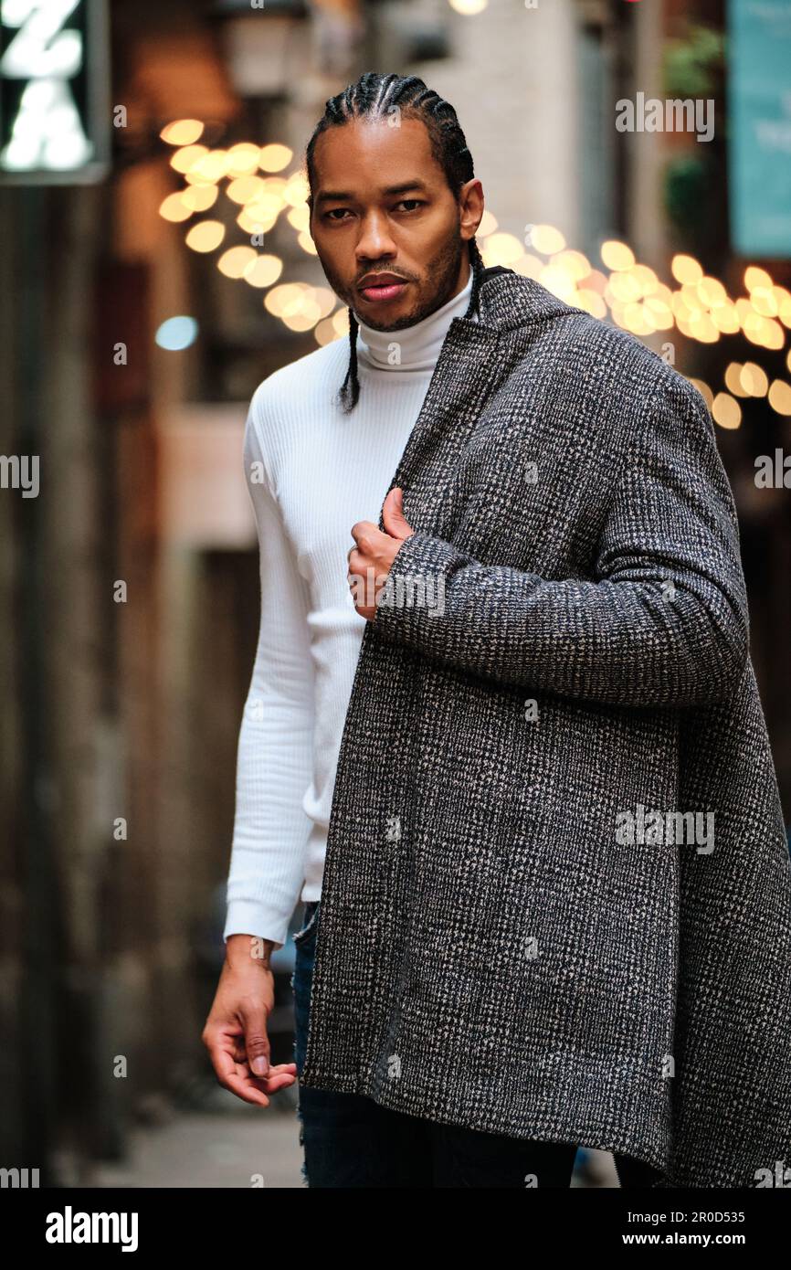 Stylish African American man looking at camera with serious face while wearing a coat standing outdoors. Stock Photo