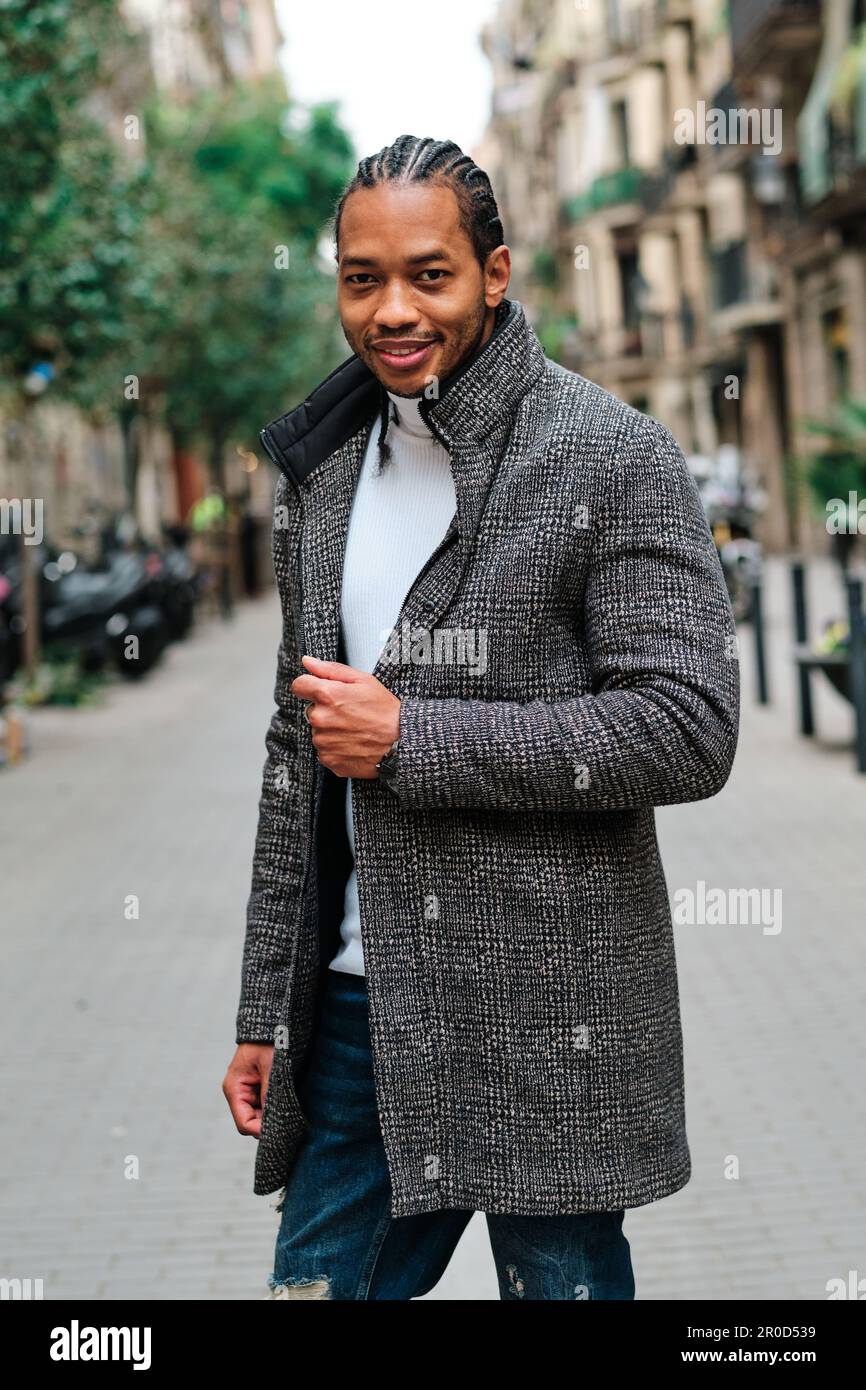 Stylish African American man with coat looking at camera and smiling while posing outdoors. Stock Photo
