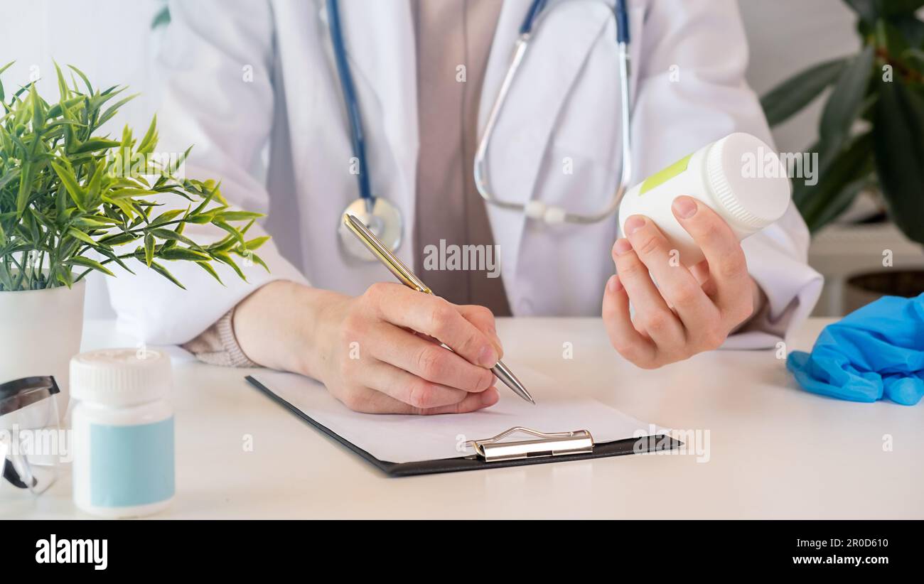 Female black medicine doctor hand hold jar of pills and write prescription to patient at worktable. Panacea and life save, prescribing treatment legal Stock Photo