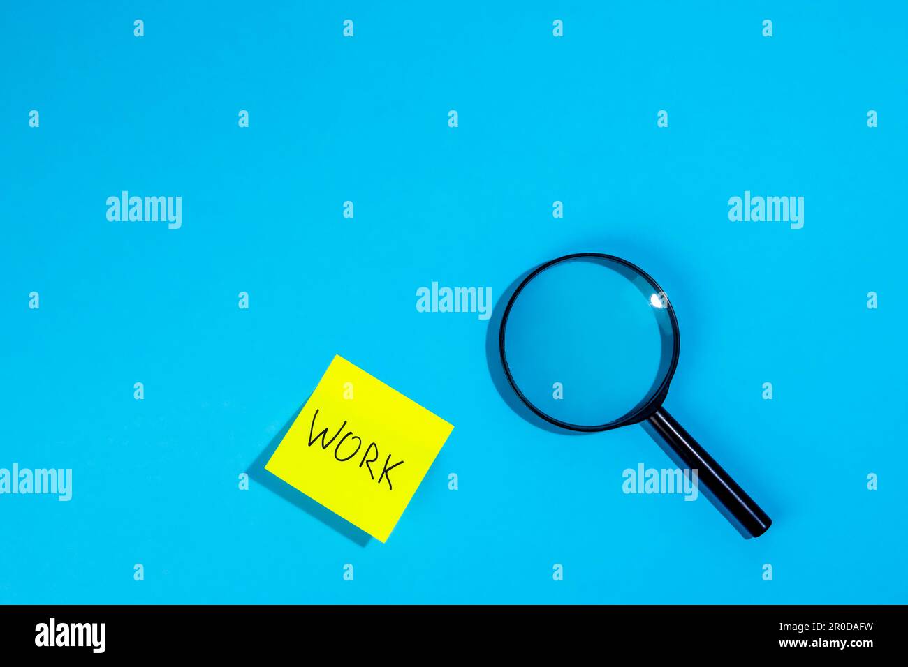 Magnifying loupe and a sticker with the word work on a blue background. Stock Photo