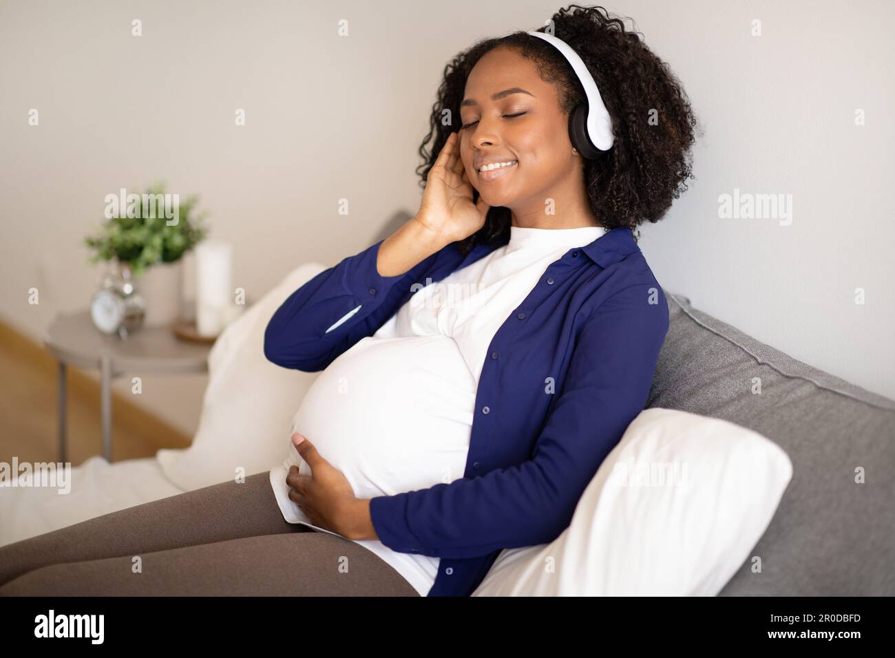 Happy millennial african american woman with big belly in headphones ...