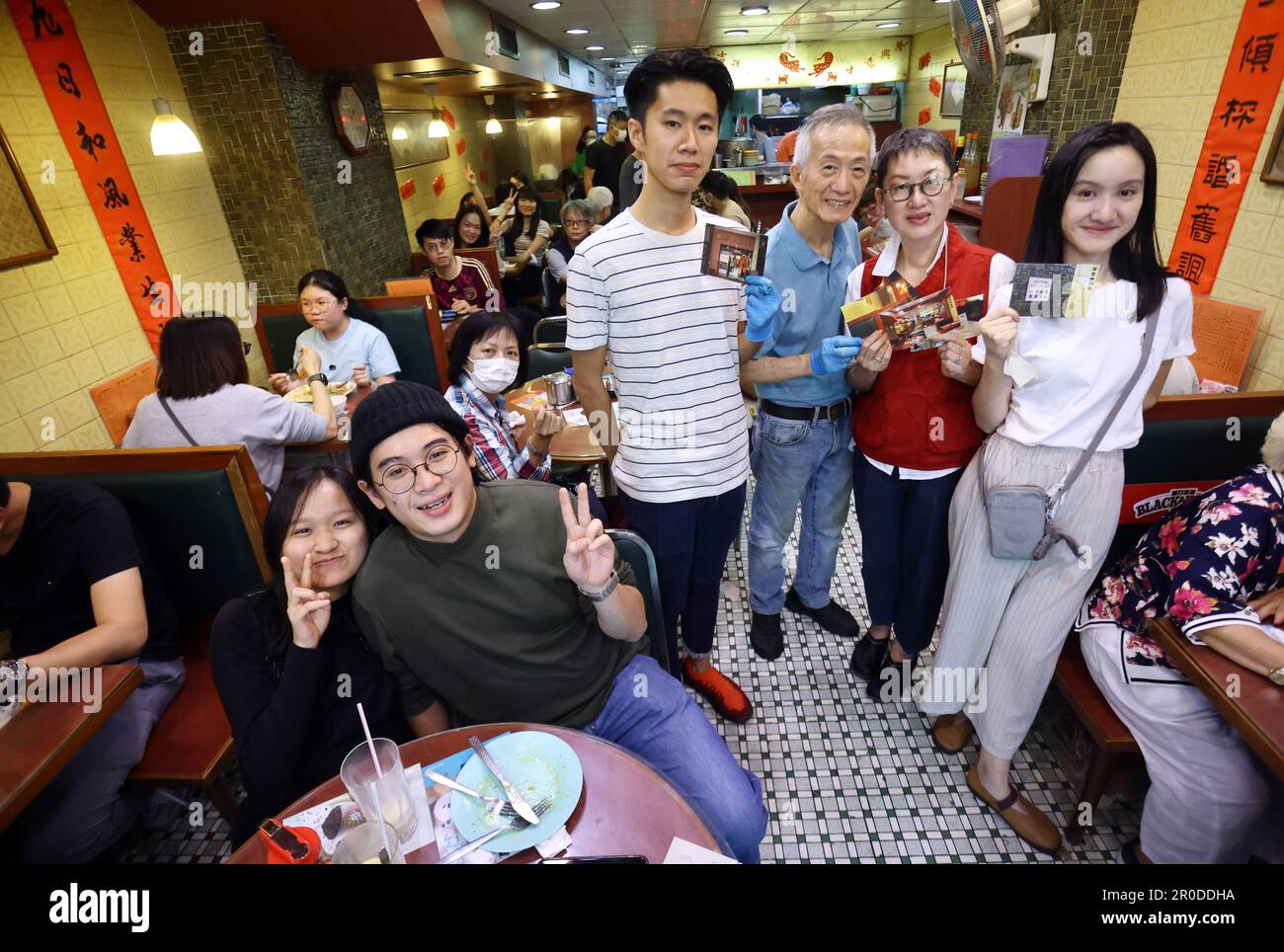 The owner family (3rd from left) Ivan Lam (son), café owner affectionately known as Mr Blue, Carol Chau among regular customers and (daughter) Terrie Lam with limited edition postcards designed by Ivan and Terrie holding in hands, pose for a photo at Yuen Fat Cafe to mark the closure of the eatery at Prince Edward today.   31OCT22.      SCMP / May Tse Stock Photo