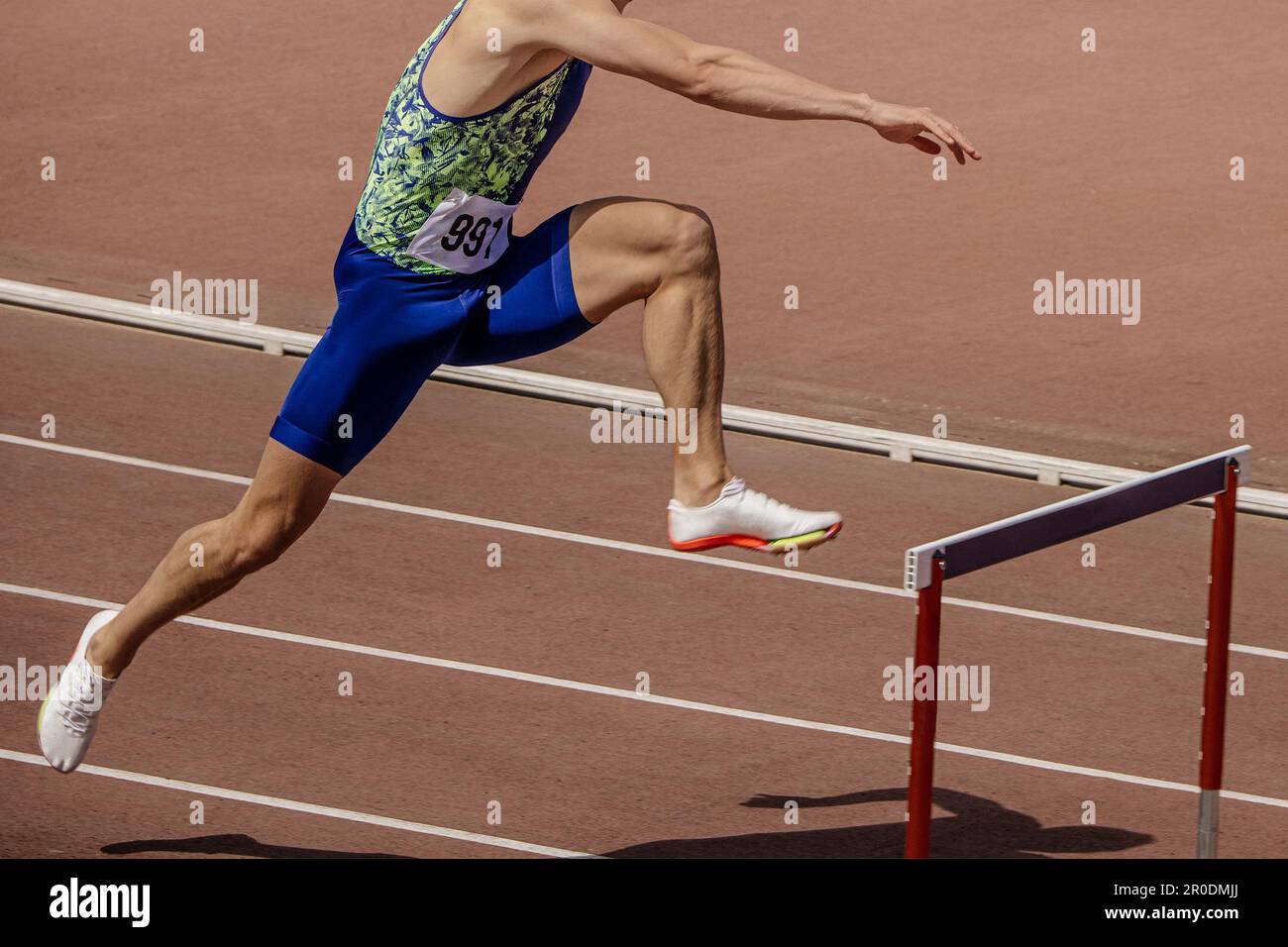 male athlete runner attack hurdle 400 meters running race in summer athletics championships side view Stock Photo