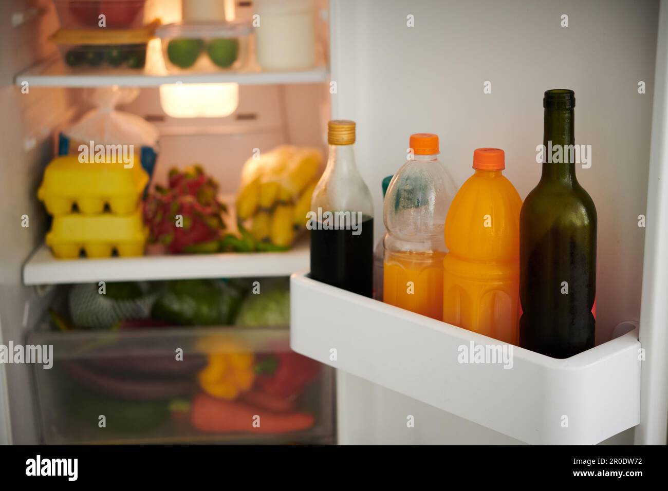 Opened fridge with bottles with wine and soft drinks, fresh fruits and veggitables Stock Photo