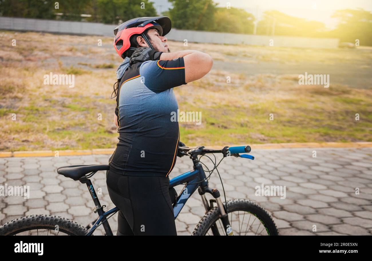 Sporty cyclist having neck pain while riding a bike. Male cyclist with neck pain outdoors Stock