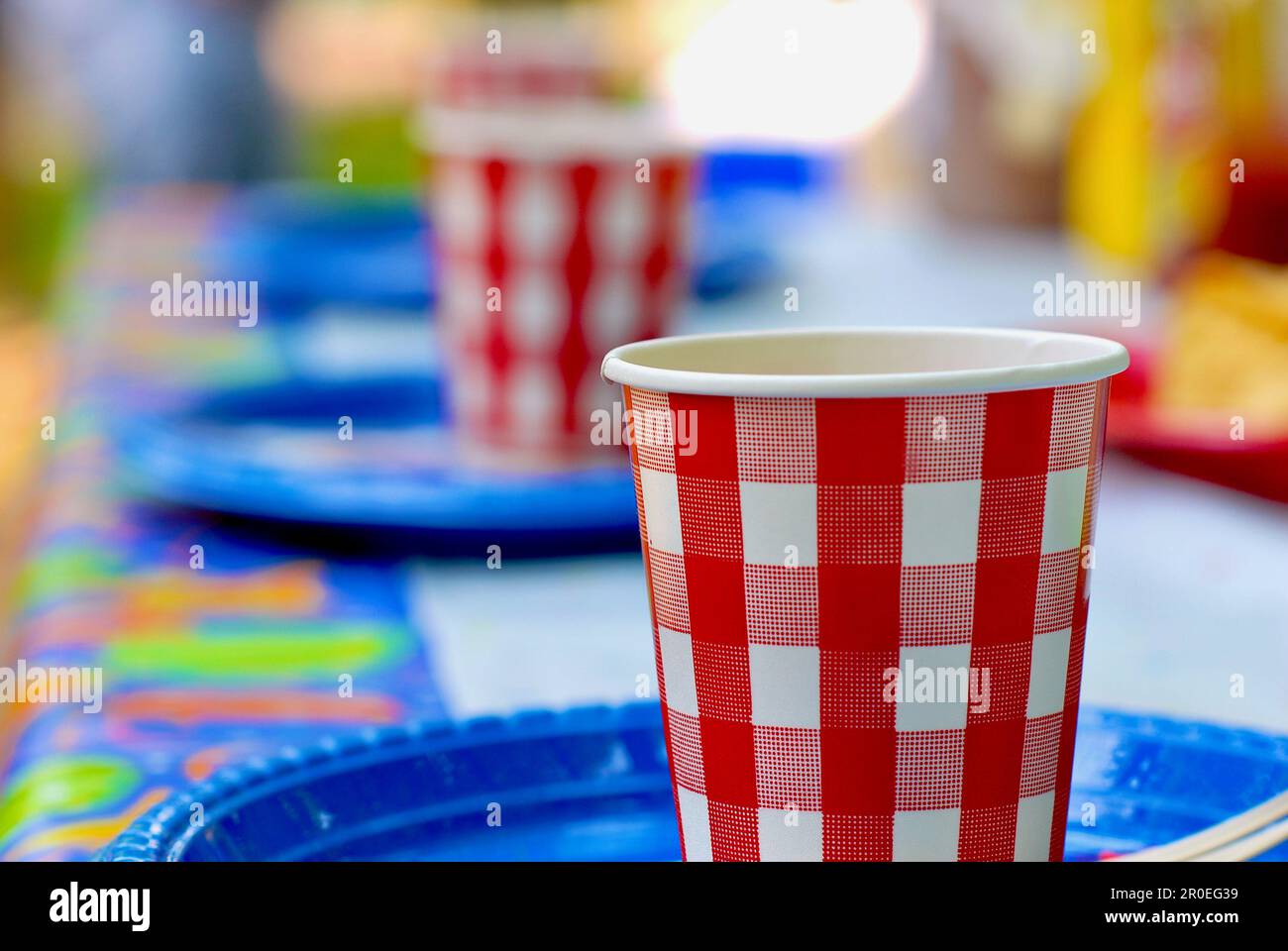 Red and white checkered paper cups sit atop blue plastic plates at a ...