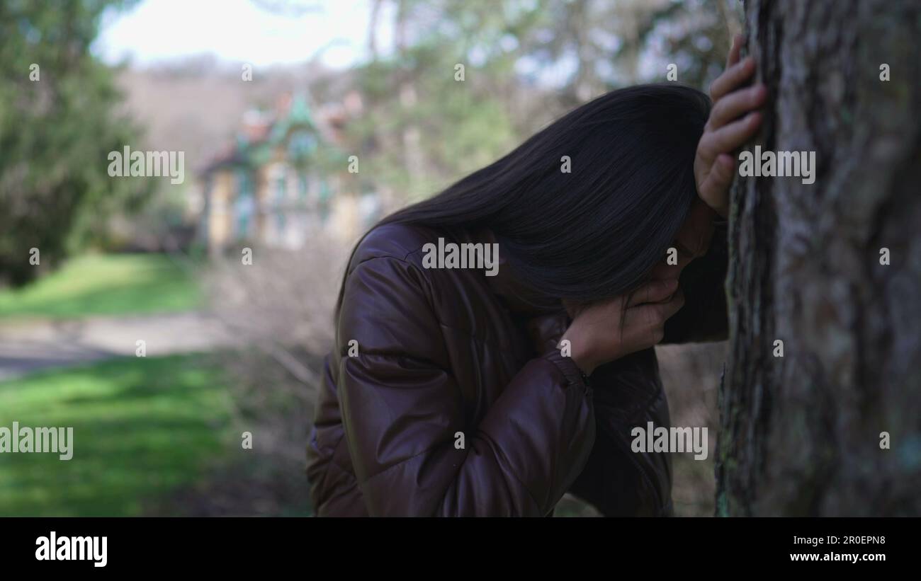 Suffering woman leaning on tree feeling nauseous covering mouth with hand. Person feels like vomiting because of traumatic regret Stock Photo