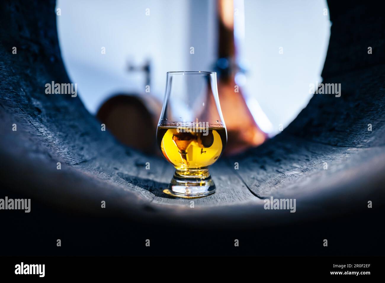 A glass of whiskey in old oak barrel. Copper alambic on background