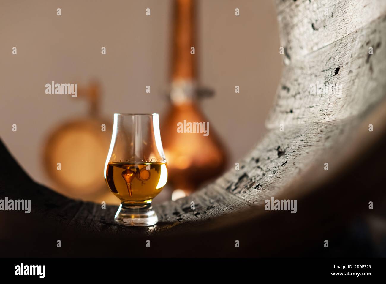A glass of whiskey in old oak barrel. Copper alambic on background
