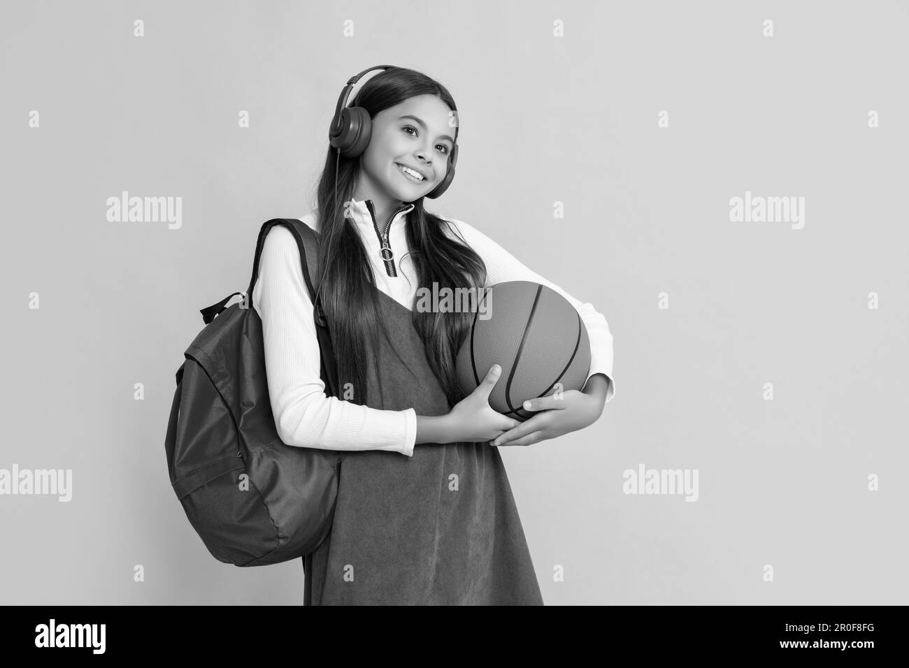 child smile in headphones with school backpack and basketball ball on yellow background Stock Photo