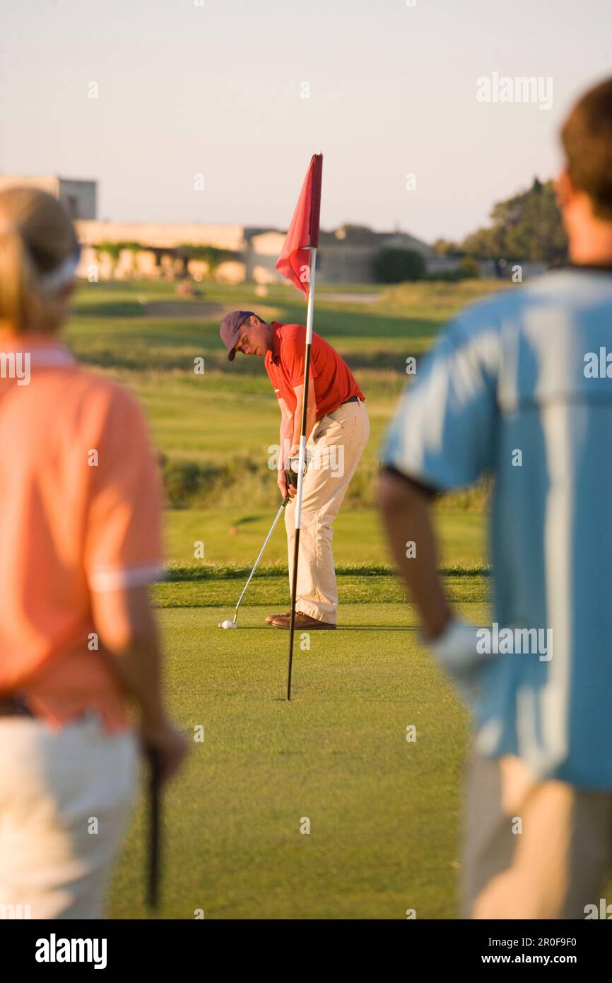 Male golfer preparing to hit ball, woman and man looking to him, Apulia, Italy Stock Photo
