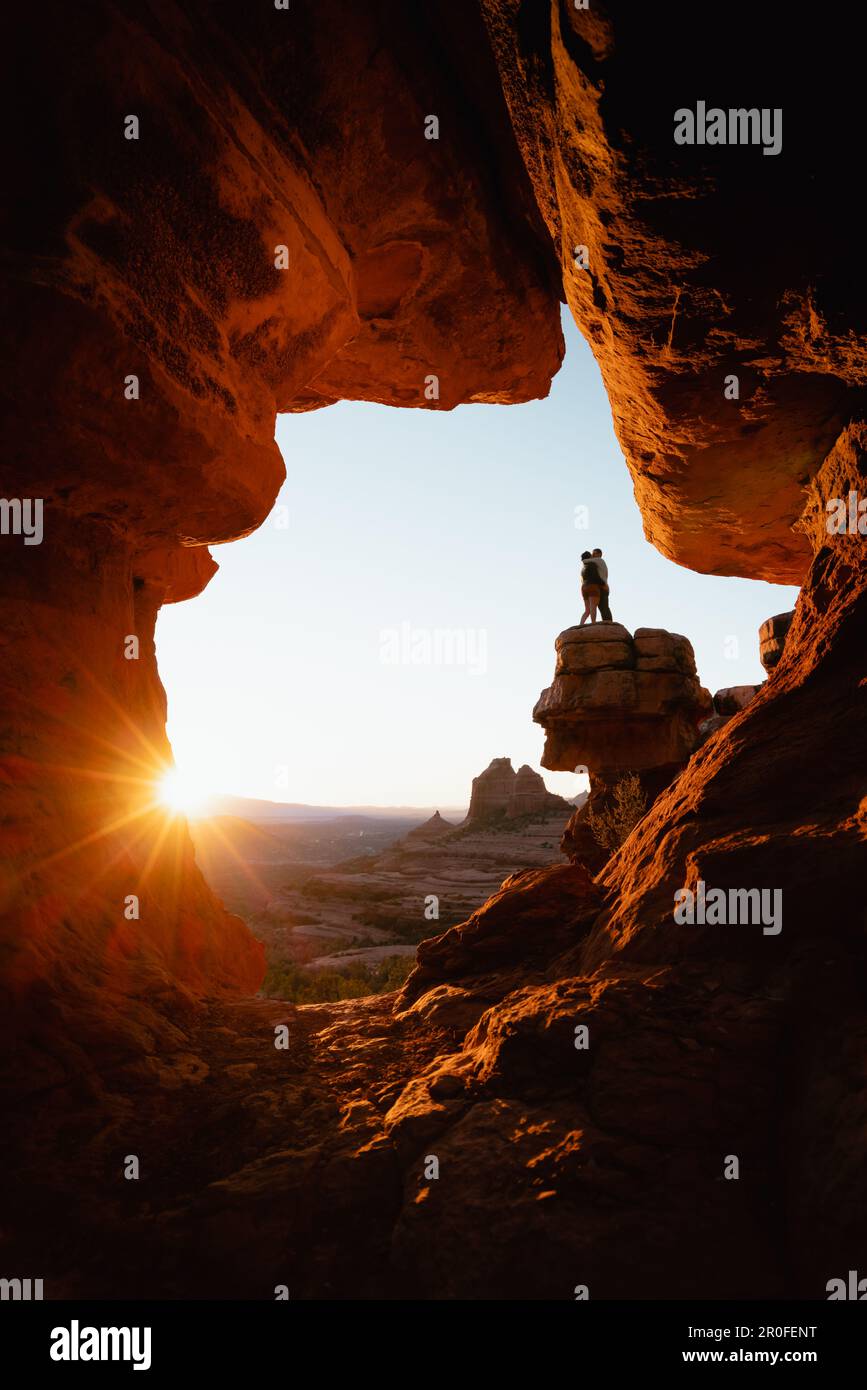 Young couple kisses at popular viewpoint rock formation in Sedona Arizona at golden orange sunset. Stock Photo