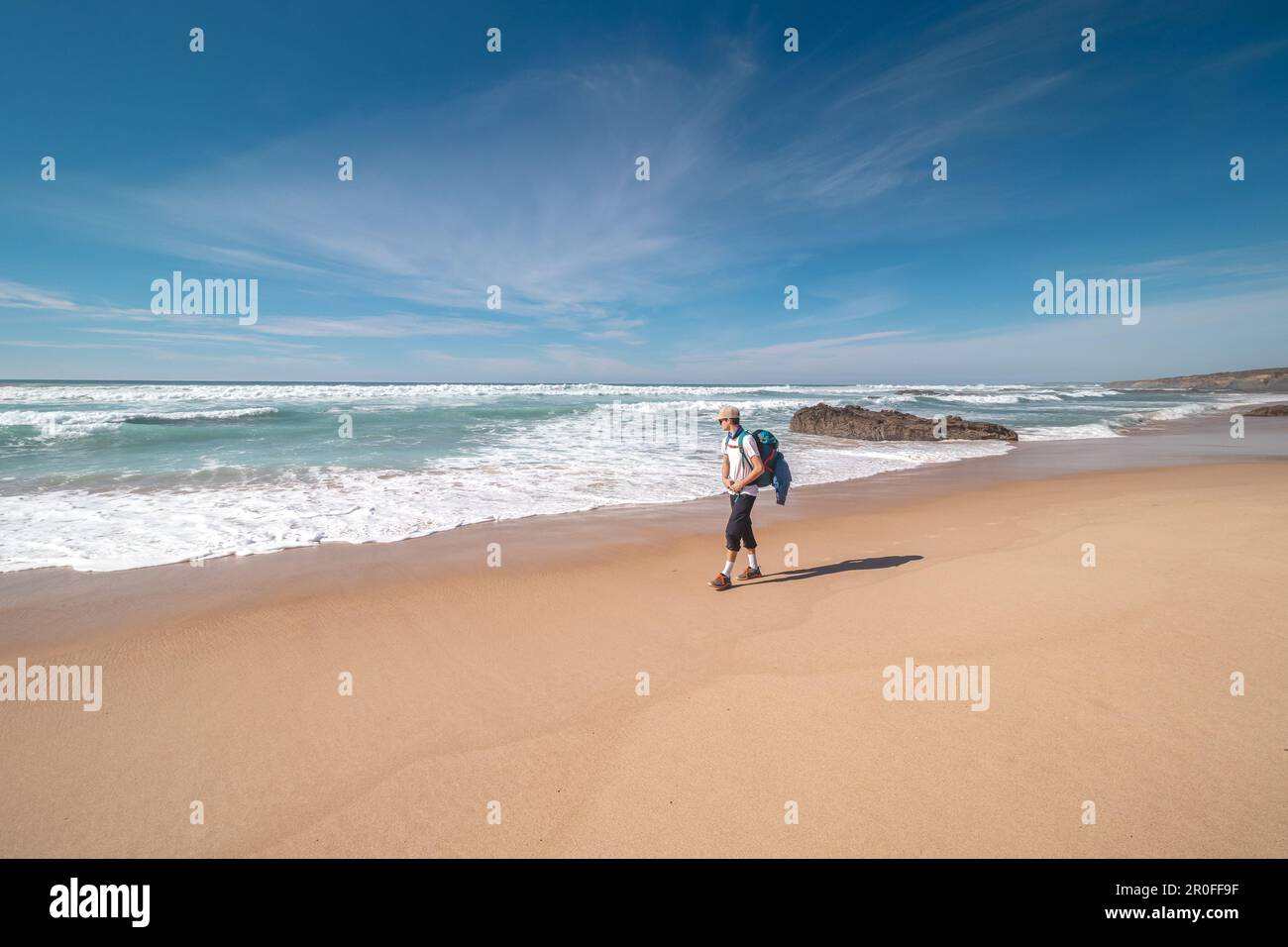 Backpacker walks along Praia do Almograve with a smile on his face. The joy of moving and discovering new places. Odemira region, western Portugal. Wa Stock Photo