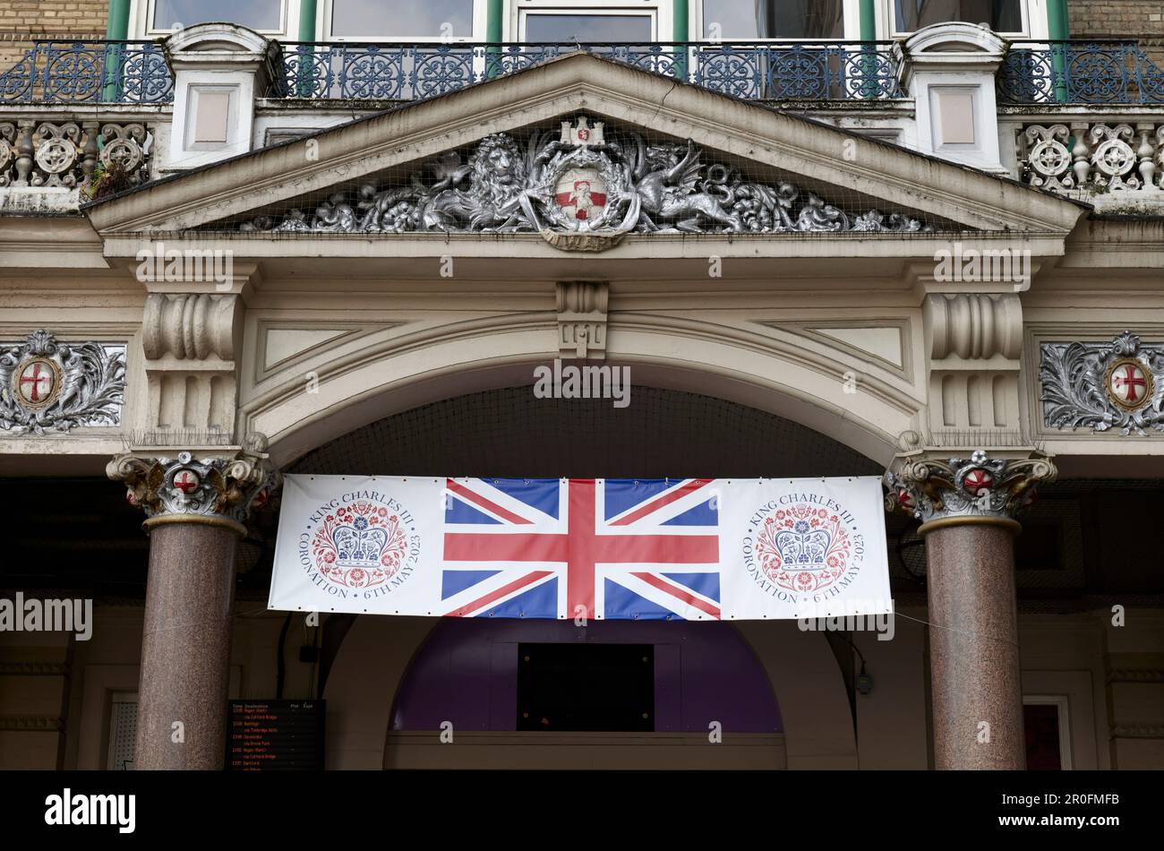 Banner for the coronation of King Charles III and Queen Camilla above an entrance to Charing Cross station, London, under the South Eastern Rly crest Stock Photo