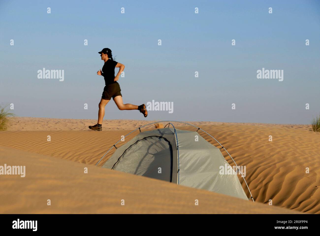 Woman jogging over dune, tent in foreground, Djebel Tembaine, Tunisia Stock Photo