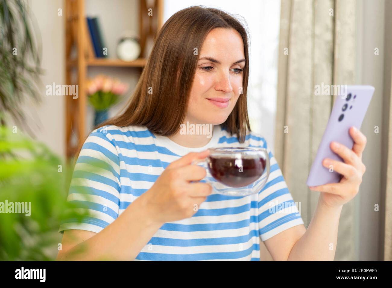 Woman sitting at table with cup of tea, chatting with friends or buying online Stock Photo