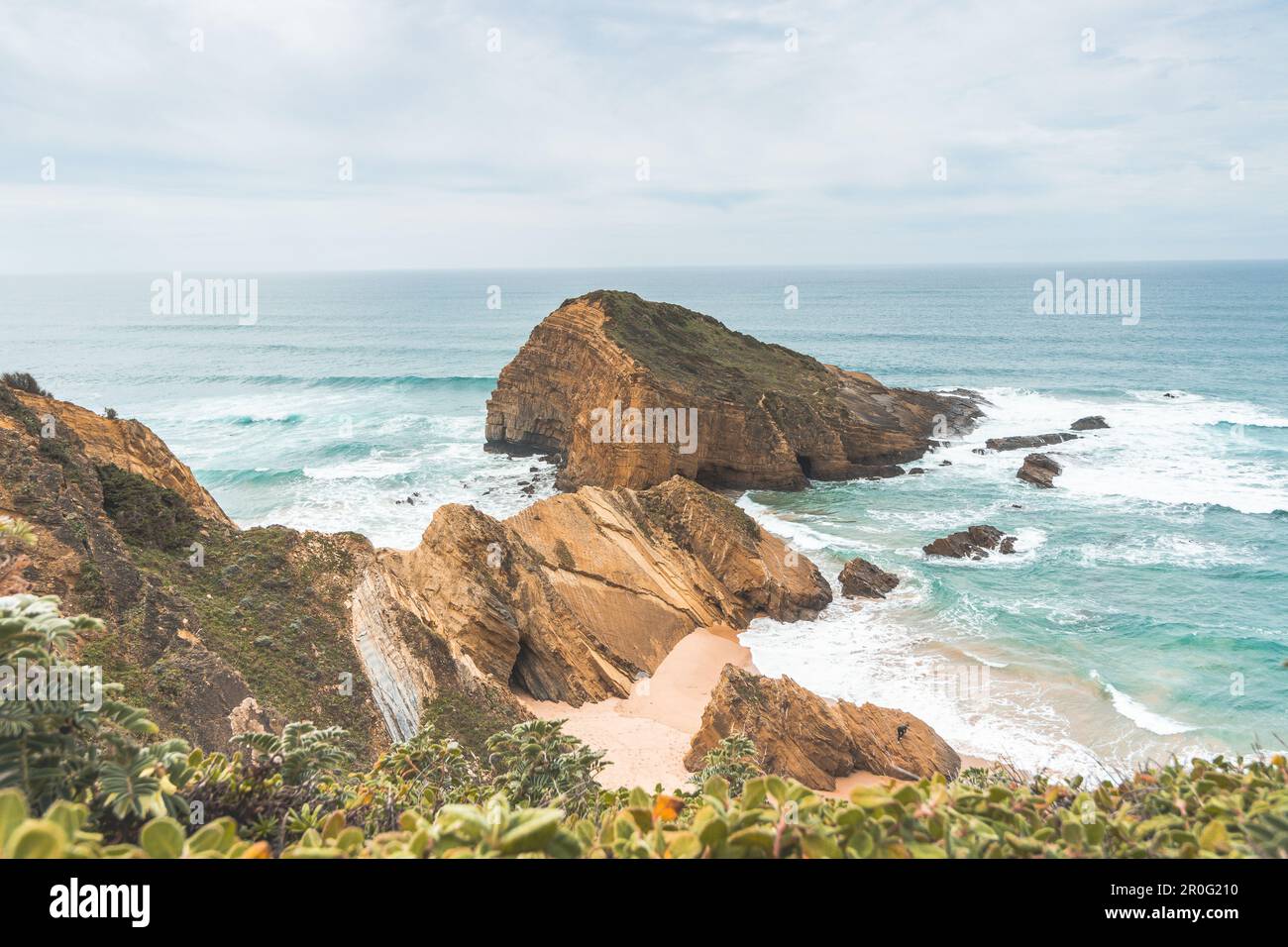 Steep cliffs plunging into the yellow-orange sand watered by the waves of the Atlantic Ocean in the region of Odemira, Portugal. In the footsteps of t Stock Photo