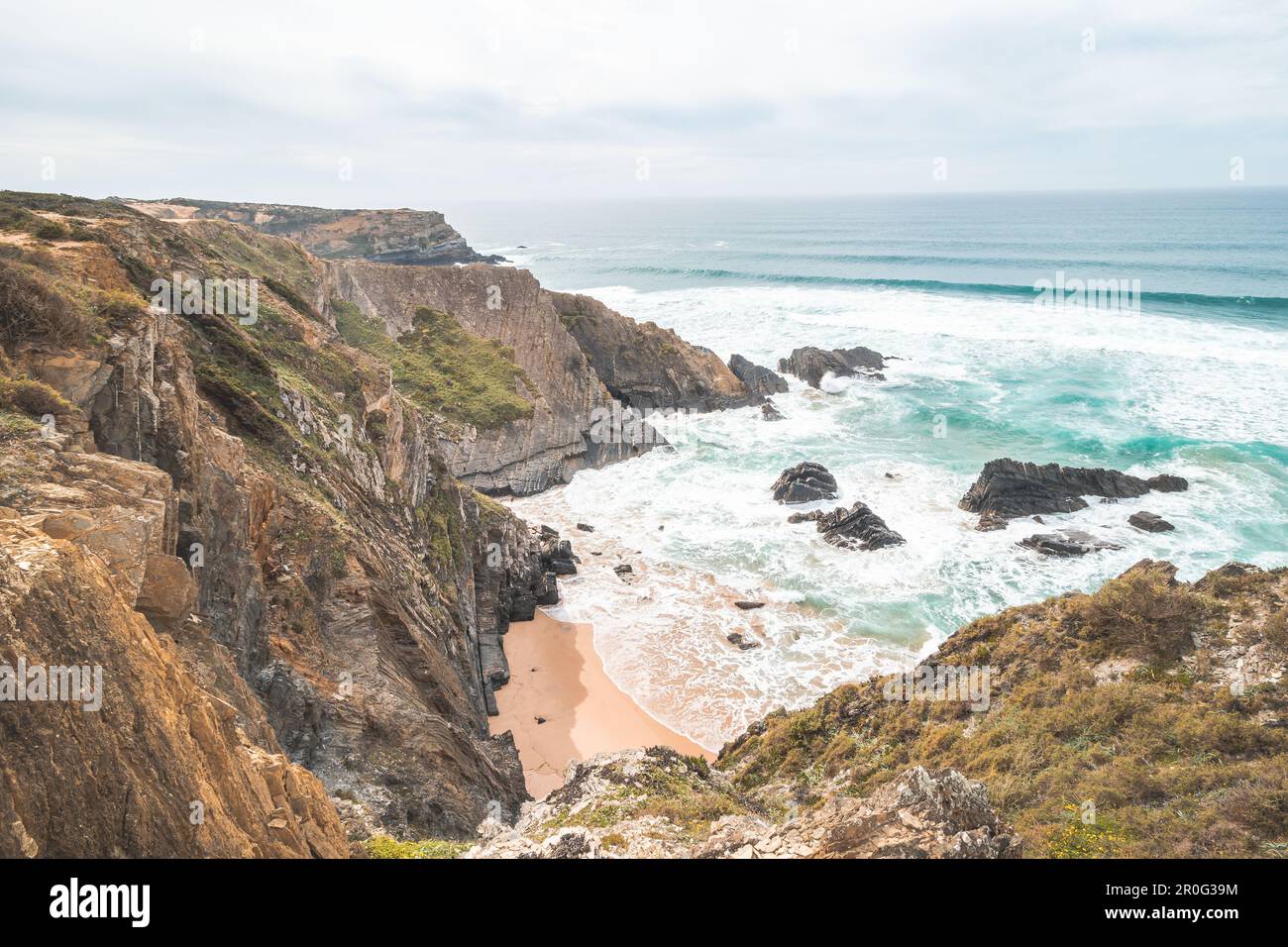 Steep cliffs plunging into the yellow-orange sand watered by the waves of the Atlantic Ocean in the region of Odemira, Portugal. In the footsteps of t Stock Photo