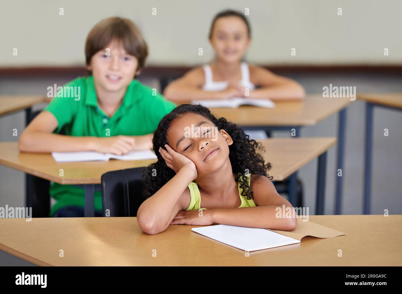 School is wearing her out. A bored looking ethnic girl sitting at her desk at school. Stock Photo