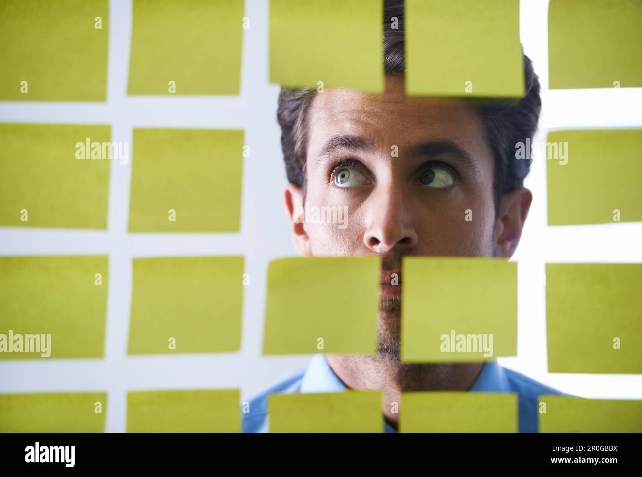 Creative man, face and thinking in sticky note for schedule brainstorming or planning tasks on glass board at office. Thoughtful male contemplating Stock Photo