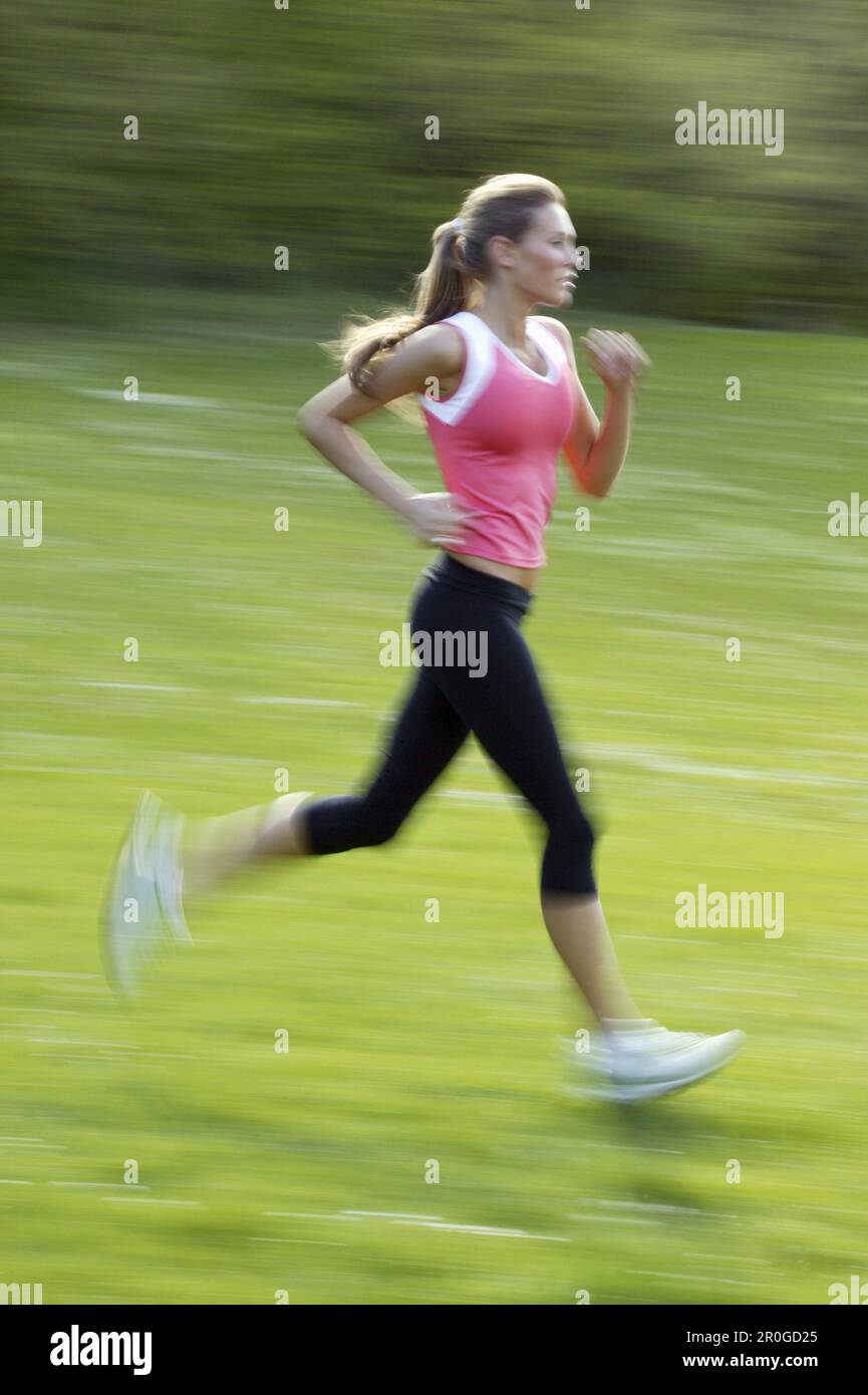 Young woman wearing a pink top, jogging through green fields, Bavaria, Germany Stock Photo