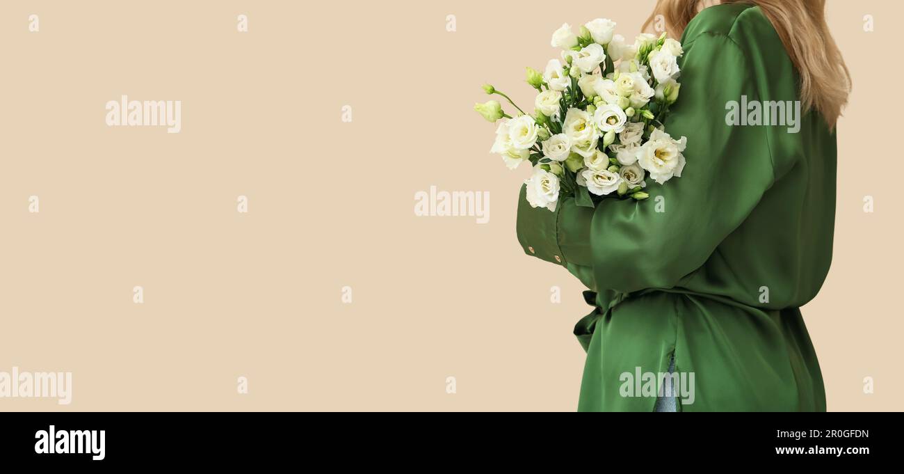 Young woman holding bouquet of beautiful eustoma flowers on beige ...