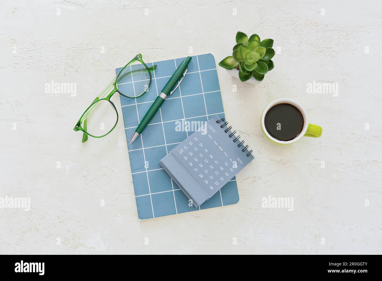 Flip paper calendar, cup of coffee, eyeglasses, houseplant and notebook ...