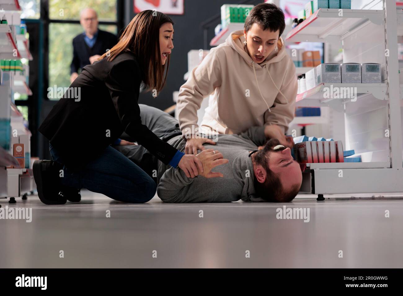 Women standing on knees near unconscious man with epilepsy lying on pharmacy retail store floor