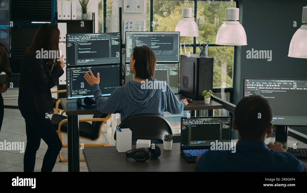 System engineer checking code on multiple monitors and working with app developer colleague in it agency office. Coder analyzing algorithm on screens, developing new user interface. Stock Photo