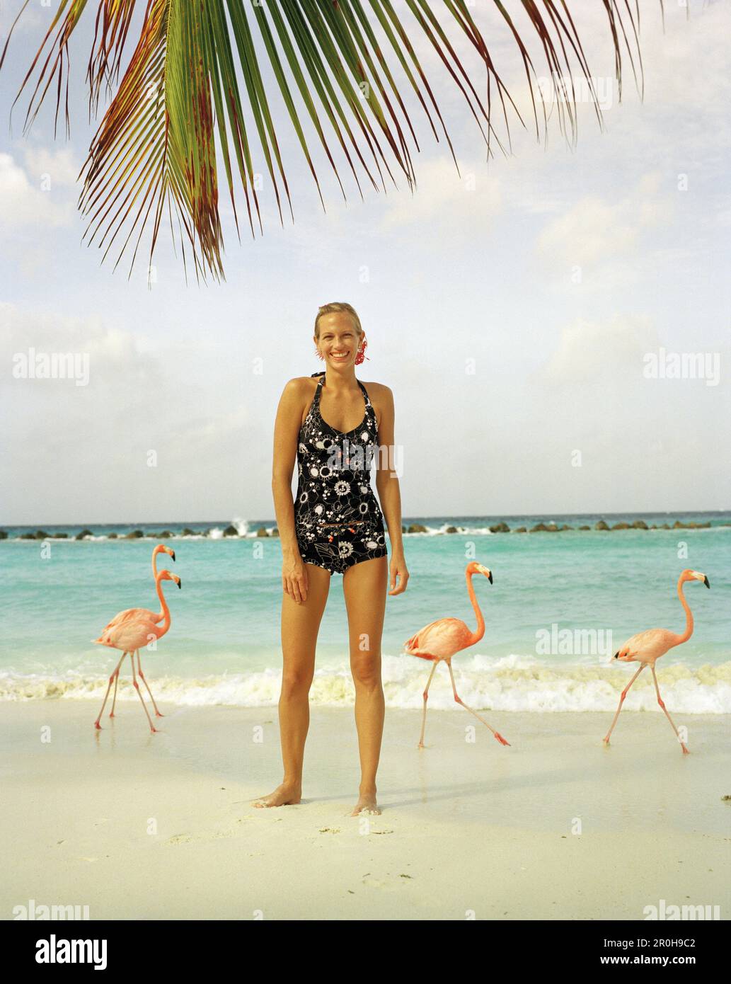 ARUBA, portrait of young woman standing on the beach smiling in the middle of Pink Flamingos, Renaissance Island Stock Photo