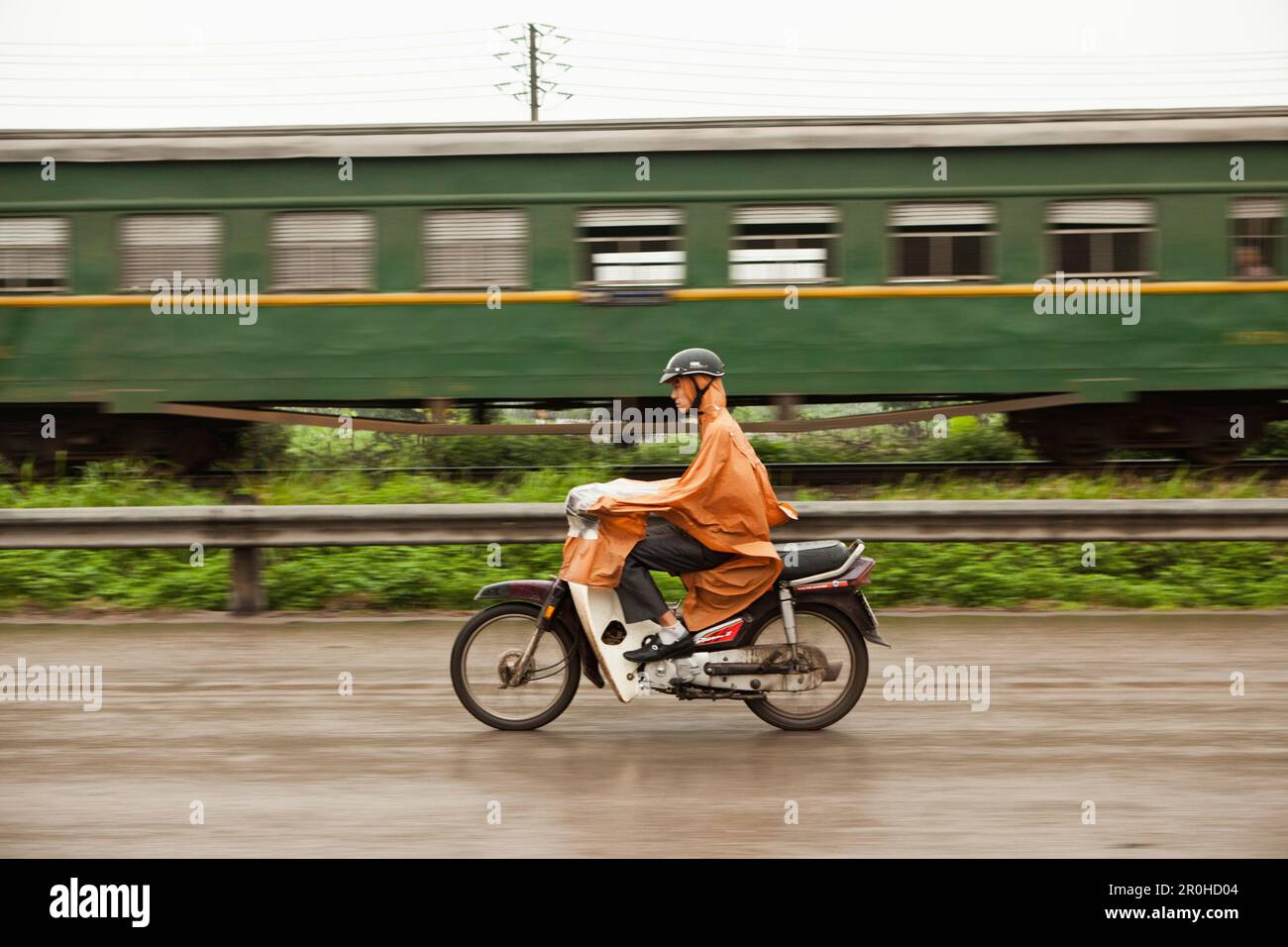 VIETNAM, Hanoi, Countryside, a man passes a train on his moped in the