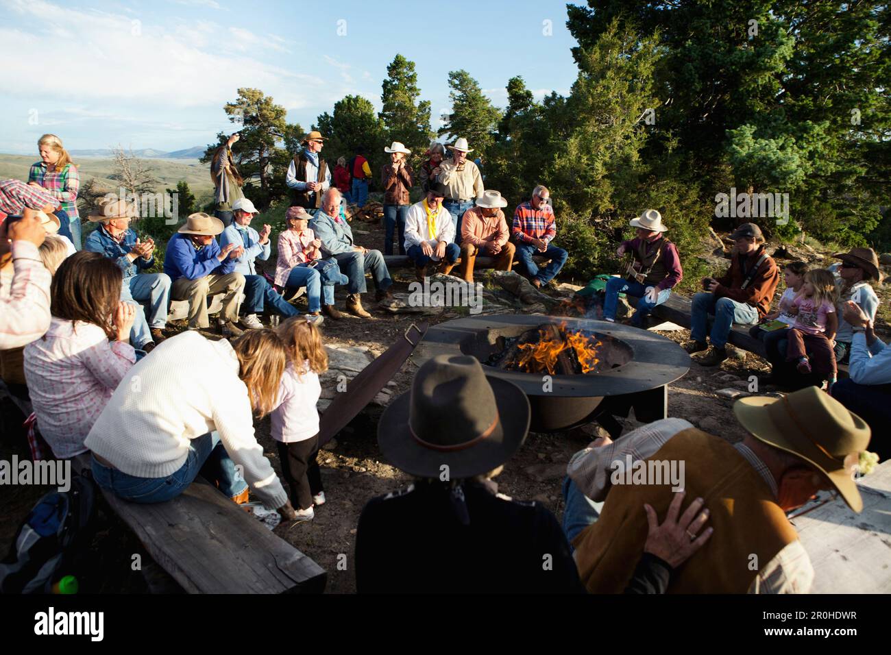 USA, Wyoming, Encampment, guests at a dude ranch sit around a campfire ...