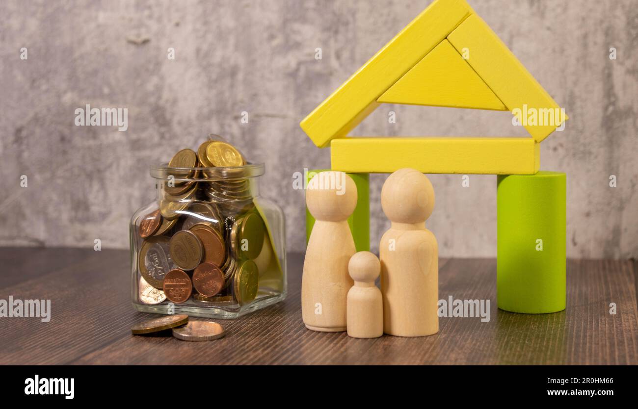 Family budget planning concept. Investments, plans, savings. Mortgage rates. Real estate. Glass jar with coins 2023 and family near the wooden house Stock Photo