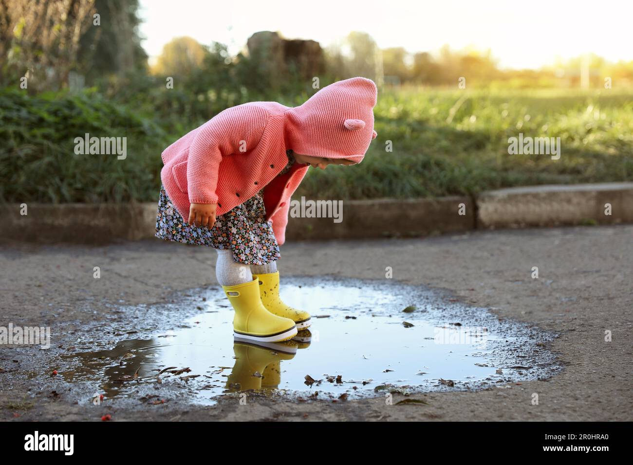 Little girl wearing rubber boots standing in puddle outdoors, space for ...