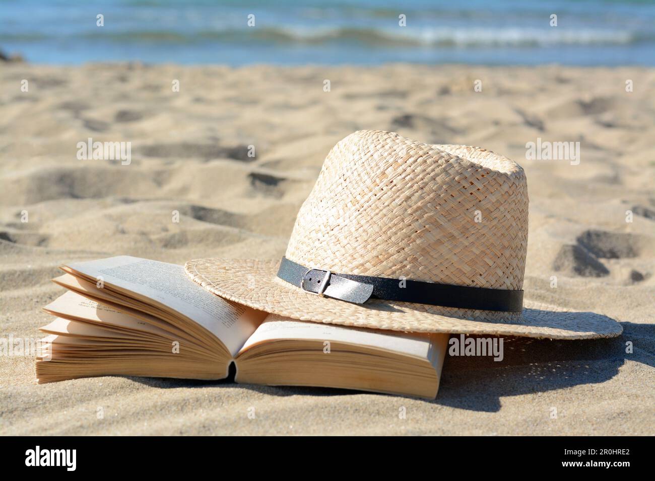 Open book and straw hat on sandy beach near sea Stock Photo - Alamy