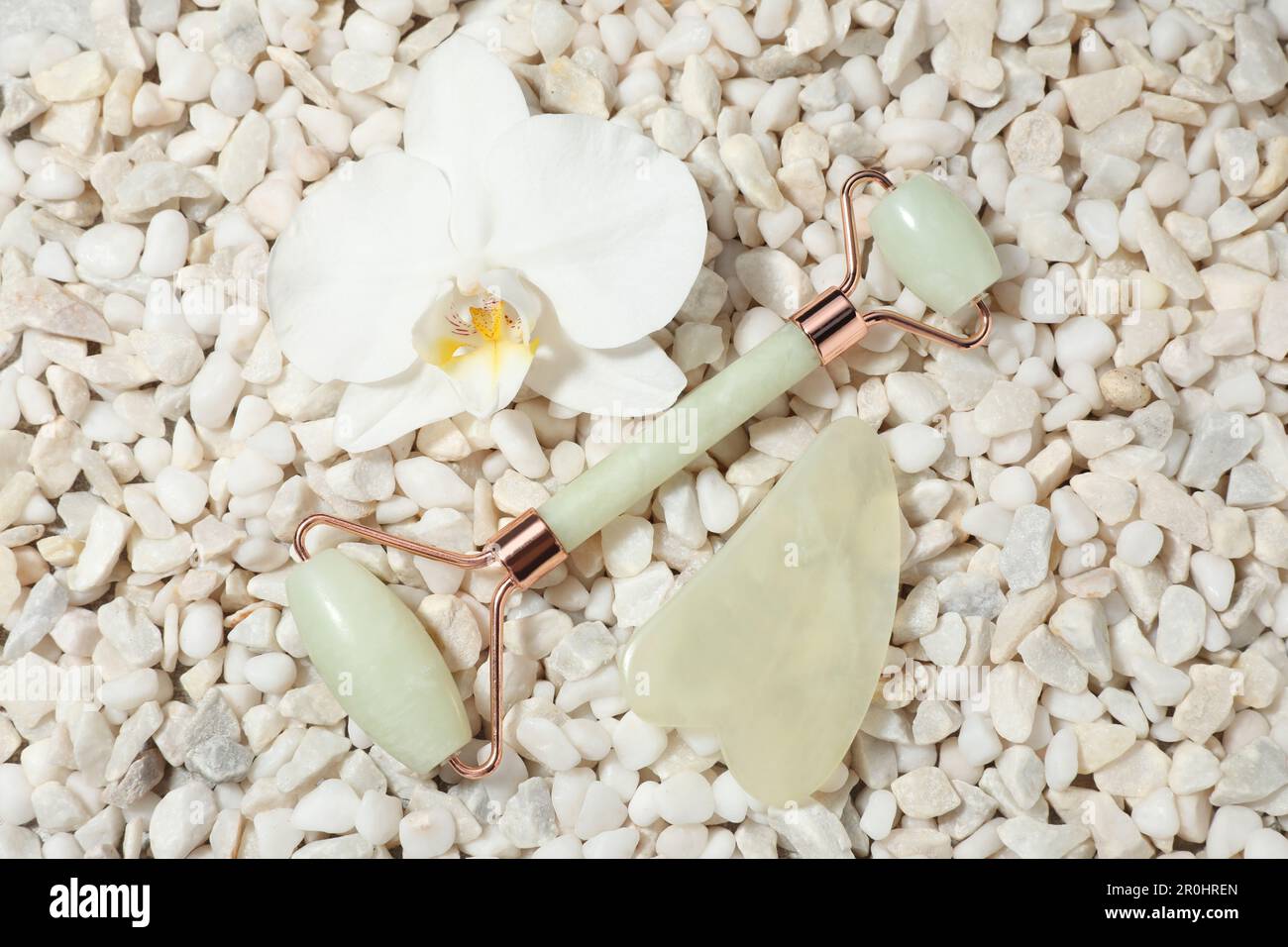 Quartz gua sha tool, face roller and orchid flower on white stones, flat lay Stock Photo