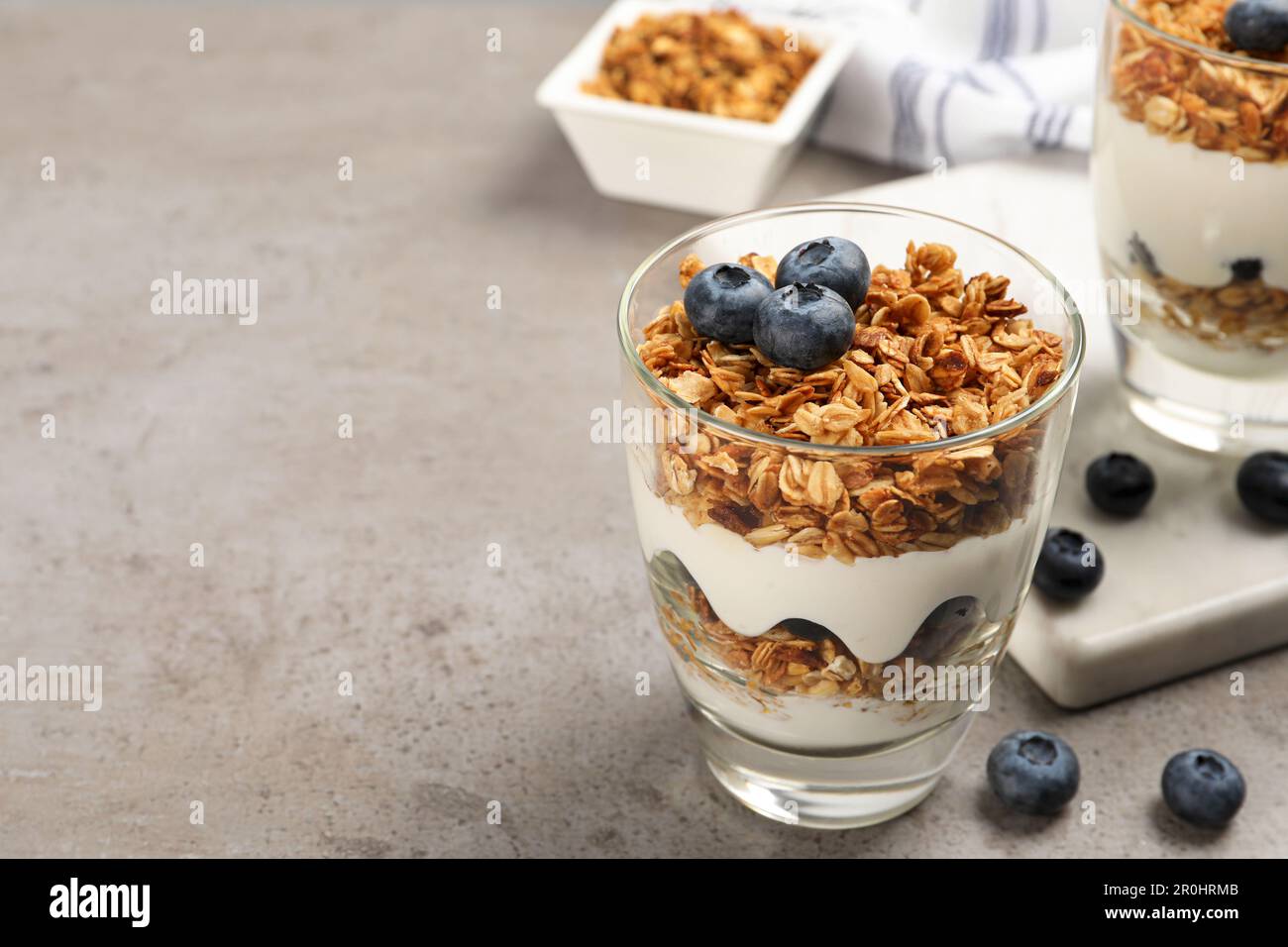 Glasses of yogurt with granola and blueberries on grey table, closeup. Space for text Stock Photo