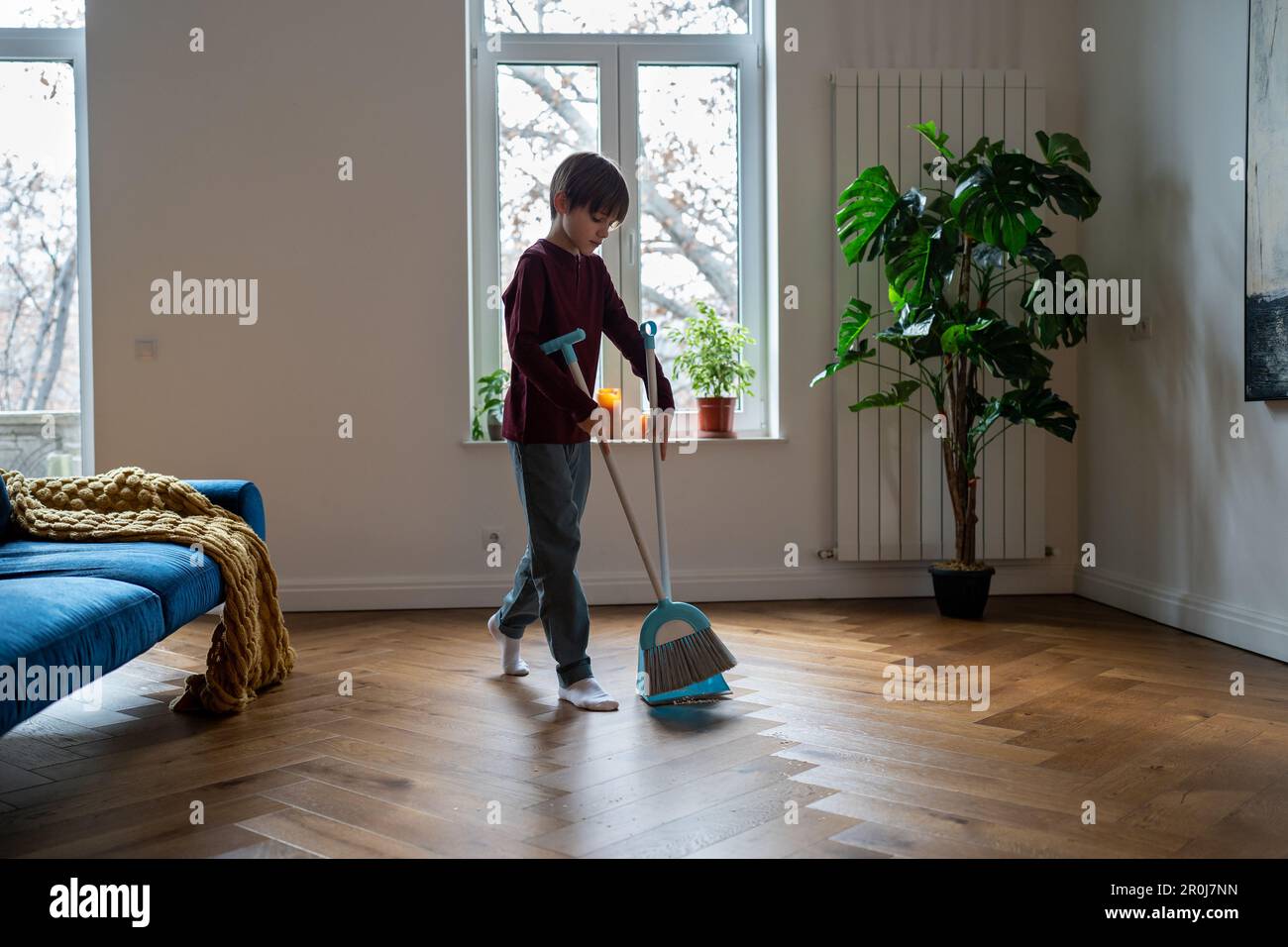 Teen boy doing chores cleaning floor in living room sweeping trash with