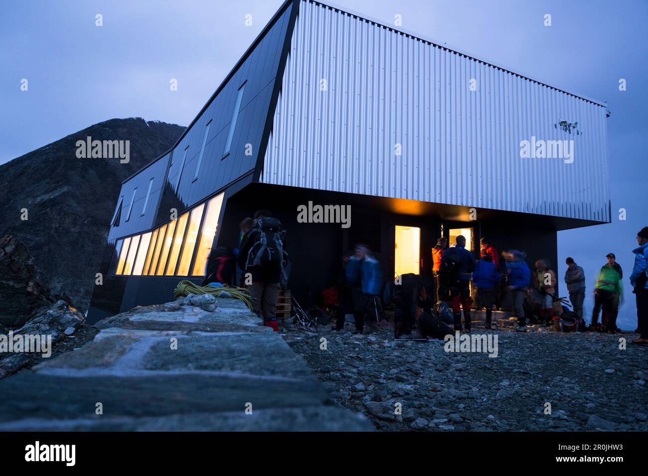 Early morning, alpinists in front of the new, modern Tracuit Hut are getting ready for the ascent of the Bishorn, while the windows of the hut are sti Stock Photo