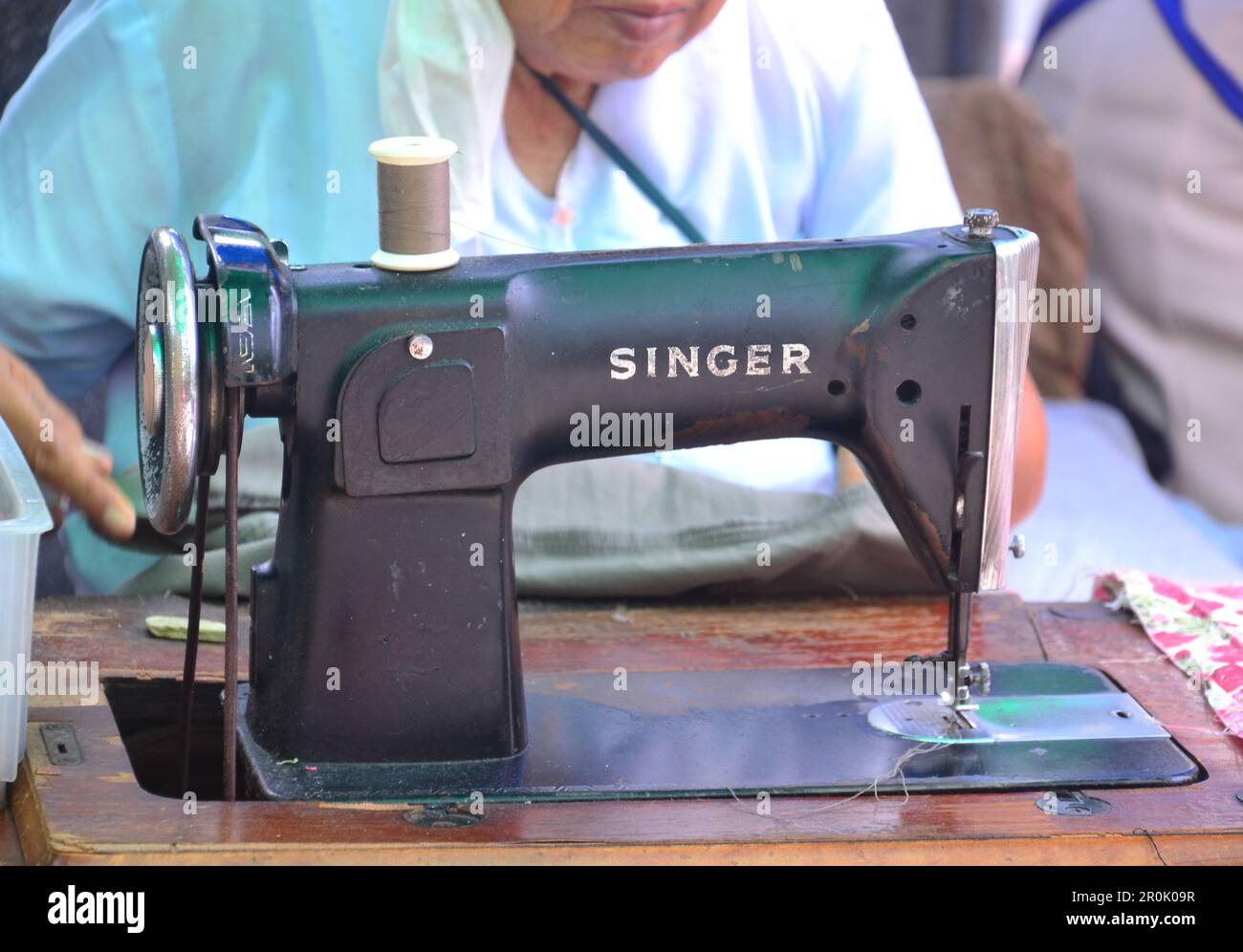 An older woman uses an old Singer sewing machine on the street in