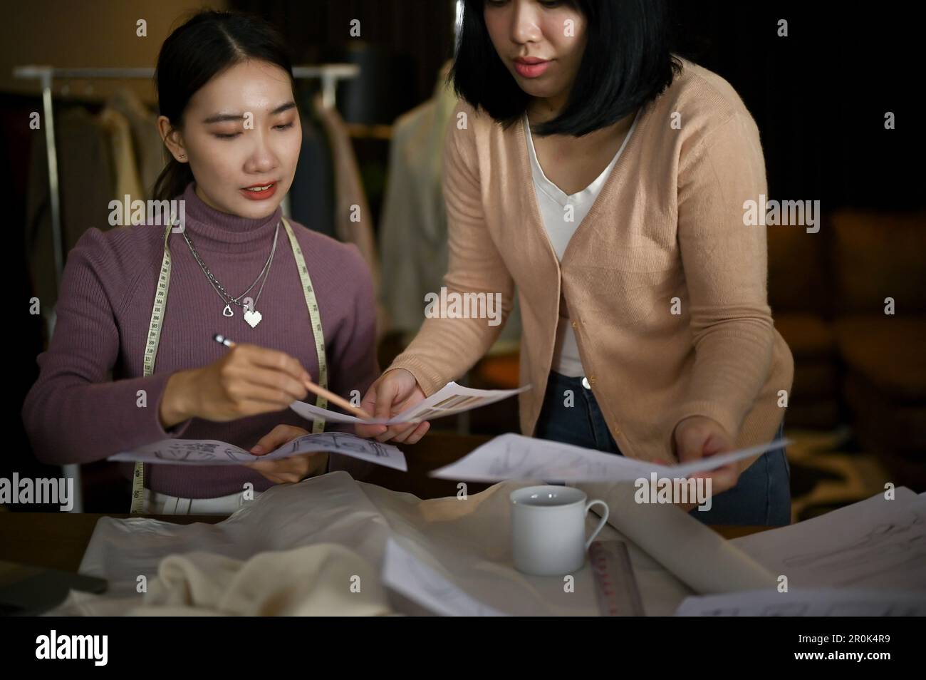 Two professional Asian female fashion designers or tailors are discussing and planning their new collection, and working in the studio together. Stock Photo