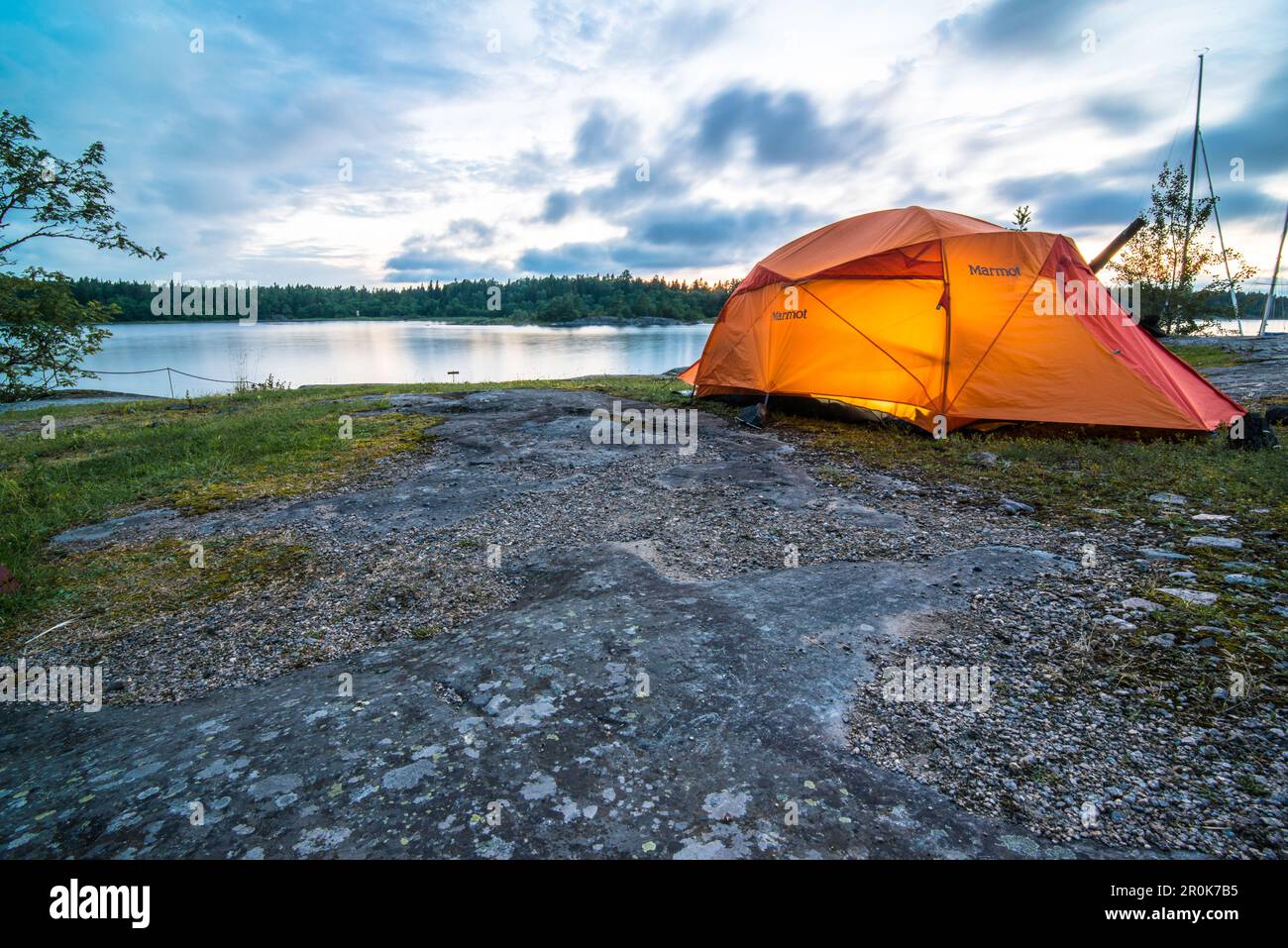 On  the rocks next to the water stands the orange glowing tent in the evening light, Anskarsclub, Oregrund, Uppsala, Sweden Stock Photo