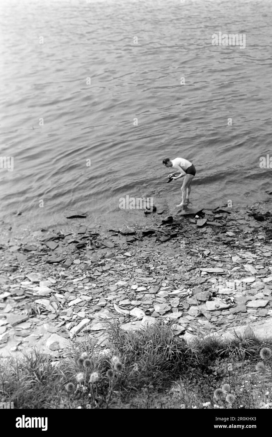 Ein Mann in Badehose wäscht seine Schuhe im Rhein bei Sankt Goarshausen, 1961. A man in swimming trunks washes his shoes in the Rhine near Sankt Goarshausen, 1961. Stock Photo
