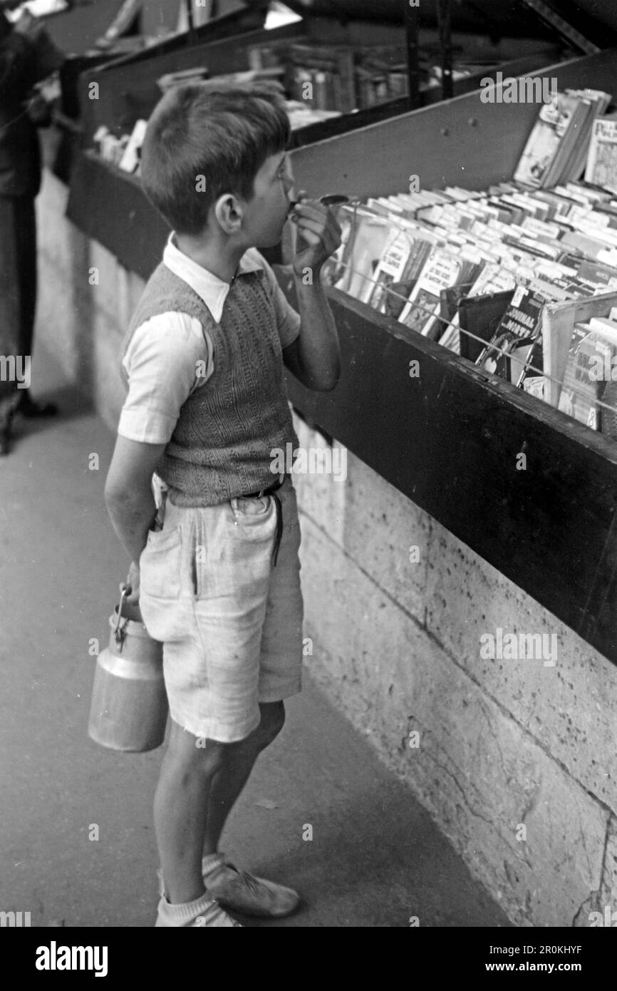 Ein Junge mit einer Milchkanne betrachtet die Comichefte in der Auslage einer Bücherbox, Paris 1940. A boy with a milk jug looks at the comic books in the display of a book box, Paris 1940. Stock Photo