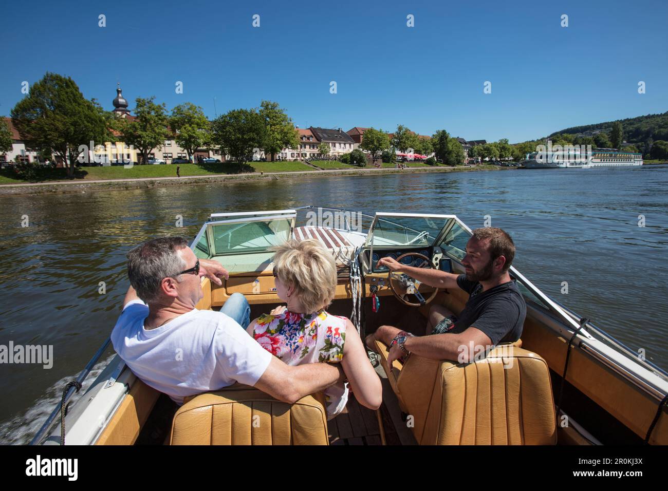 People enjoy motor boat excursion along Main river with river cruise ship Swiss Crown (Phoenix Kreuzfahrten) in distance, Marktheidenfeld, Spessart-Ma Stock Photo