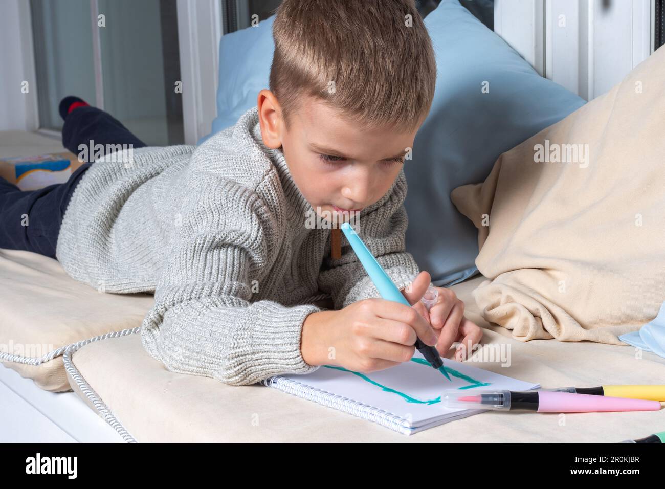 child draws on paper with felt-tip pens lying on the floor. Child doing school lesson at home. Child Education Concept, Kid Boy Drawing and Dreaming S Stock Photo