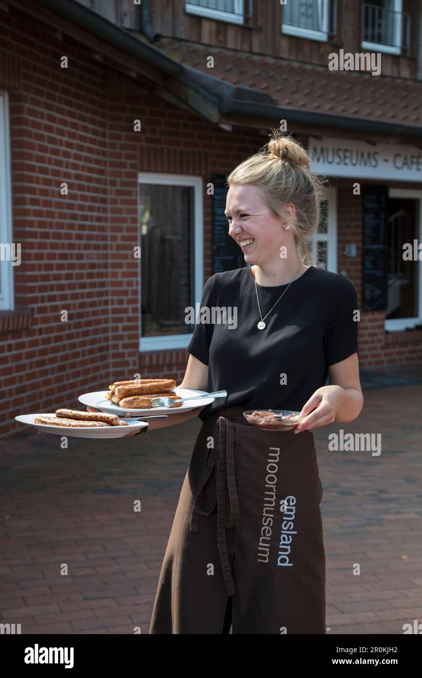 Friendly waitress serves buckwheat pancakes and sausages at Museums-Café restaurant at Emsland Moormuseum peatlands museum, Groß Hesepe, near Twist, E Stock Photo